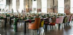 a long table with many chairs and plants on it in a large room filled with windows