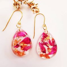 two pairs of pink and gold earrings with flowers on the top, one is hanging from hooks