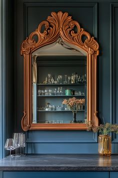 an ornate wooden mirror on the wall above a table with wine glasses and vases