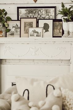 a white fireplace with pictures on the mantle and potted plants in front of it