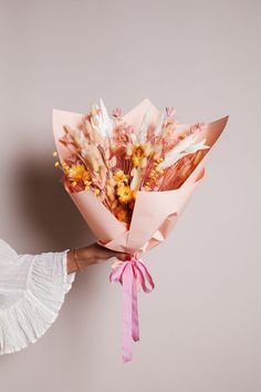 a woman holding a bouquet of flowers with pink ribbon tied around her wrist and wearing a white dress