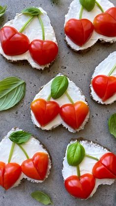 small crackers decorated with tomatoes, cheese and green leaves on a baking sheet in the shape of hearts