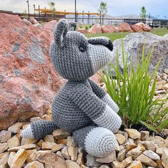 a crocheted teddy bear sitting on top of rocks next to a rock garden