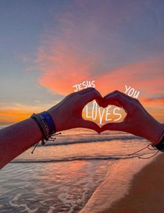 two hands making a heart shape with the word jesus loves written on it at sunset