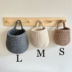 three crocheted baskets hanging on a wall with the letters l m s below them