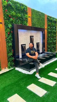 a man sitting on top of a bench in front of a wall covered with plants