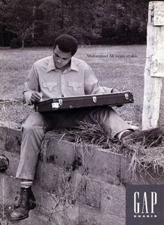 a man sitting on top of a brick wall holding a suit case in his hands