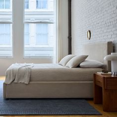 a bed sitting in the middle of a bedroom next to two windows with white brick walls