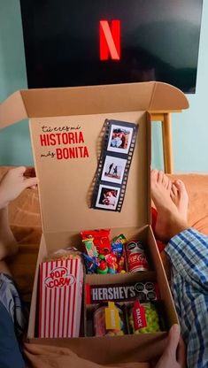 a person laying on a bed with a box full of food and snacks in it