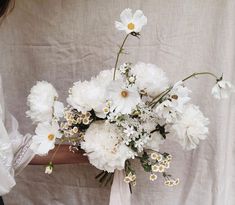 a woman holding a bouquet of white flowers in her hand on a plain cloth background