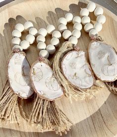 three pieces of wood with white beads and tassels on a wooden platter