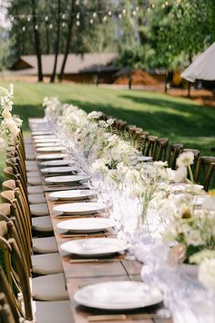 a long table is set with white flowers and place settings for an outdoor dinner party