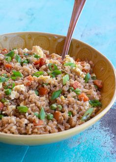 a bowl filled with rice and vegetables on top of a blue table next to a wooden spoon