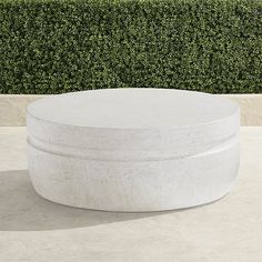 a round concrete table sitting on top of a cement floor next to a green hedge