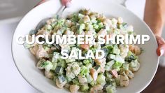 a person holding a white plate with cucumber shrimp salad on it and the words cucumber shrimp salad above it