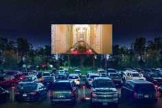 an outdoor movie screen in the middle of a parking lot filled with cars at night