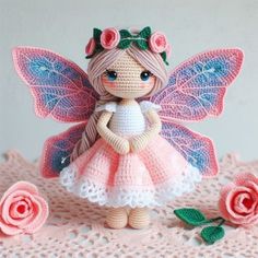 a crocheted fairy doll standing next to pink roses on a lace doily