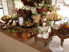 an assortment of food on a table at a wedding or other function with flowers in the background