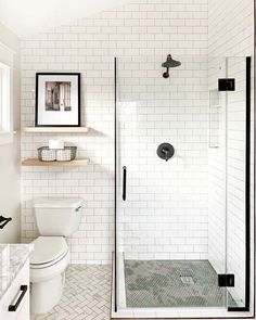 a white tiled bathroom with black accents and glass shower door, open shelving above the toilet