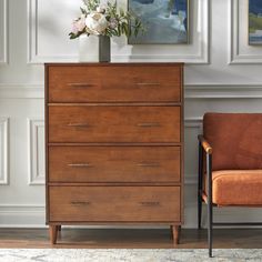 a tall wooden dresser sitting next to an orange chair in a room with paintings on the wall