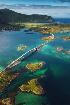 an aerial view of a bridge spanning over the ocean with mountains in the back ground