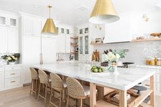 a large kitchen with white cabinets and marble counter tops, gold pendant lights over the island