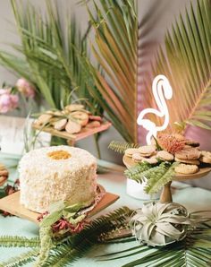 a table topped with cakes and desserts next to palm leaves