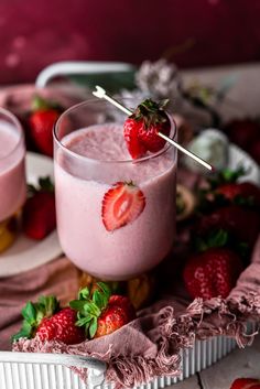 two glasses filled with strawberry smoothie on top of a white plate next to strawberries