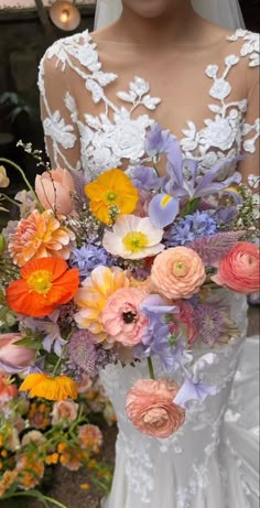 a woman holding a bouquet of flowers in her hands and wearing a wedding dress with sheer sleeves