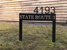 a black sign that reads state route 3 sits in front of a wooden wall and grass