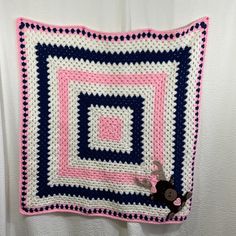 a crocheted blanket hanging on the wall with a stuffed animal in front of it