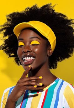 a woman with bright yellow nail polish on her face and afro hair wearing a baseball cap