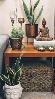 a buddha statue sitting on top of a wooden table next to a gray couch and potted plants