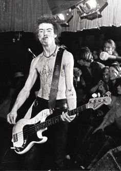 black and white photograph of a man with tattoos on his chest holding a bass guitar