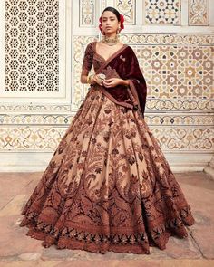 a woman in a brown and gold gown standing against a wall with intricate designs on it