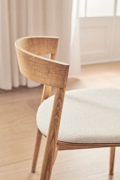 a wooden chair sitting on top of a hard wood floor next to a white curtain