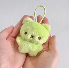 a hand holding a green teddy bear keychain in it's left hand