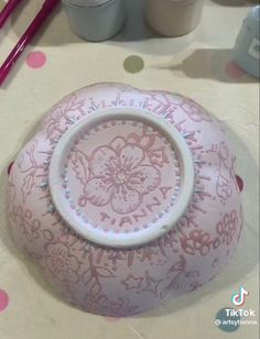 a pink vase sitting on top of a table next to some paint and pencils