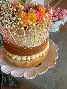 a cake with candles and flowers on it is sitting on a plate in front of other cakes