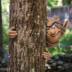 a tree with a statue of a troll peeking out from behind the trunk of a tree