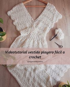 a white crochet dress sitting on top of a wooden floor next to a plant