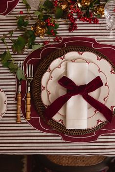 the place setting is set with red and white plates, silverware, and holly leaves