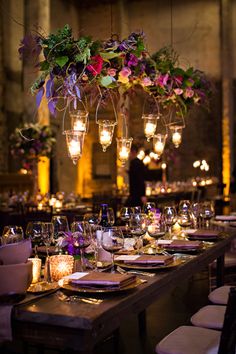 a long table is set with candles, plates and flowers hanging from the chandelier