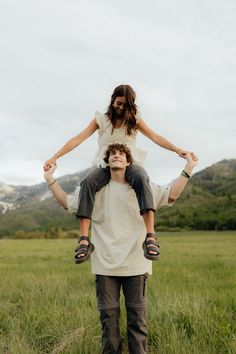 a man is balancing a woman on his shoulders in the middle of a grassy field