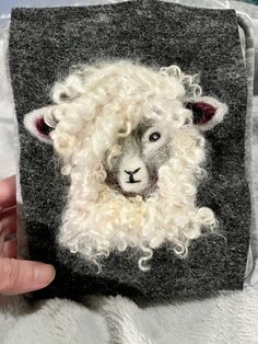 a hand holding up a small felt sheep with curly hair on it's face