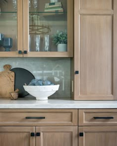 a white bowl sitting on top of a counter next to a wooden cabinet filled with glasses