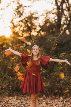 a girl in a red dress is throwing leaves into the air and smiling at the camera