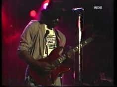 a man holding a red guitar in front of a microphone on stage at a concert