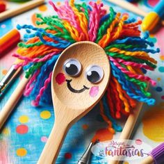 a wooden spoon with some colorful yarn on it and two crayons next to it