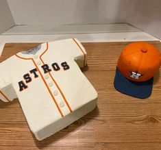 a cake shaped like a baseball jersey and hat on a wooden floor next to it